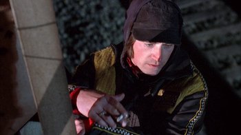 Movie still from “Paranoid Park” (2007), directed by Gus Van Sant – A man wearing a black hat and a black jacket is smoking a cigarette; Close Up shot, Low angle