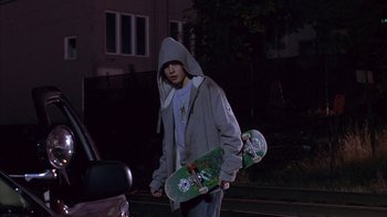 Movie still from “Paranoid Park” (2007), directed by Gus Van Sant – A young man holding a skateboard in front of a parked car; Medium shot, Low angle