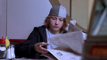 Movie still from “Paranoid Park” (2007), directed by Gus Van Sant – A young man reading a newspaper wearing a baseball cap; Close Up shot, Low angle