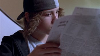 Movie still from “Paranoid Park” (2007), directed by Gus Van Sant – A young man reading a newspaper while wearing a hat; Close Up shot, Over the shoulder angle