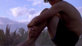 Movie still from “Paranoid Park” (2007), directed by Gus Van Sant – A man sitting on the ground with his legs crossed; Medium shot, Low angle