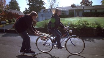 Movie still from “Paranoid Park” (2007), directed by Gus Van Sant – A man and a woman riding a bike and skateboard down a street; Wide shot, Low angle