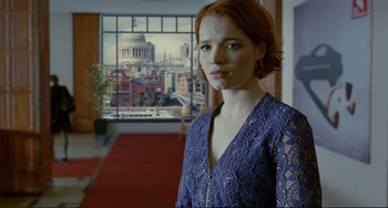 Movie still from “Passion” (2012), directed by Brian De Palma – A woman standing in front of a window with a city view; Medium shot, Over the shoulder angle