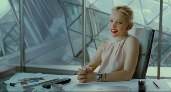 Movie still from “Passion” (2012), directed by Brian De Palma – A woman sitting at a table with a remote control; Medium shot, Over the shoulder angle