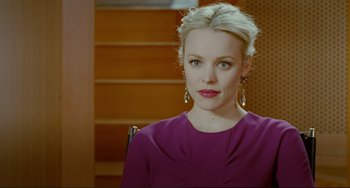 Movie still from “Passion” (2012), directed by Brian De Palma – A woman in a purple dress sitting in front of a staircase; Close Up shot, Over the shoulder angle