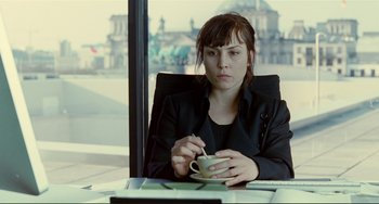 Movie still from “Passion” (2012), directed by Brian De Palma – A woman sitting at a table holding a cup of coffee; Medium shot, Over the shoulder angle