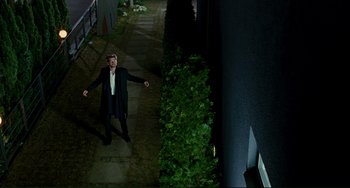 Movie still from “Passion” (2012), directed by Brian De Palma – A man standing on a sidewalk near a bush; Wide shot, High angle