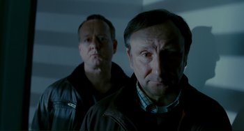 Movie still from “Passion” (2012), directed by Brian De Palma – Two men standing next to each other in front of a wall; Close Up shot, Low angle