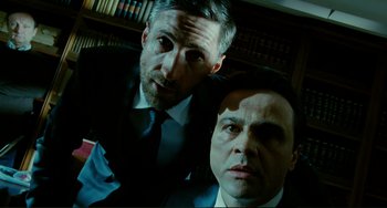 Movie still from “Passion” (2012), directed by Brian De Palma – A couple of men standing next to each other in a room; Close Up shot, Low angle