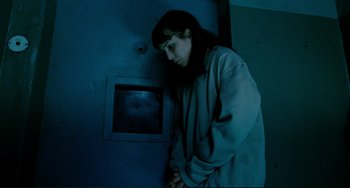 Movie still from “Passion” (2012), directed by Brian De Palma – A woman leaning against a wall in a dark room; Medium shot, High angle