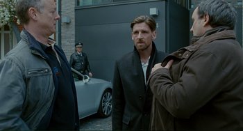 Movie still from “Passion” (2012), directed by Brian De Palma – A man standing next to two other men in front of a car; Medium shot, Over the shoulder angle