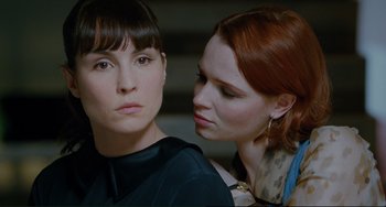 Movie still from “Passion” (2012), directed by Brian De Palma – Two women looking at each other with one of the women holding her hand on the other; Close Up shot, Over the shoulder angle
