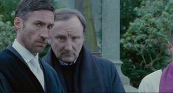 Movie still from “Passion” (2012), directed by Brian De Palma – Two men standing next to each other in front of a building; Close Up shot, Over the shoulder angle