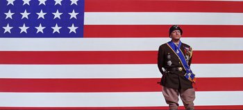 Movie still from “Patton” (1970), directed by Franklin J. Schaffner – A man in a uniform stands in front of an american flag; Wide shot, Low angle
