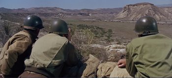 Movie still from “Patton” (1970), directed by Franklin J. Schaffner – A man in a helmet is sitting on a rock looking out over a valley; Wide shot, Over the shoulder angle