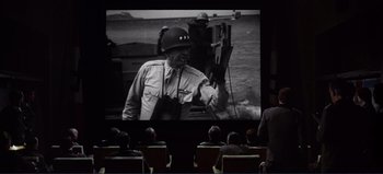 Movie still from “Patton” (1970), directed by Franklin J. Schaffner – People sitting in chairs watching a movie on a big screen; Wide shot, High angle