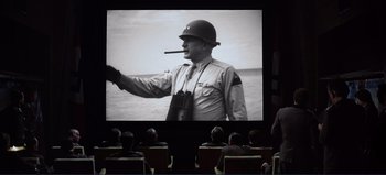 Movie still from “Patton” (1970), directed by Franklin J. Schaffner – People sitting in front of a large screen with an image of a man smoking a cigar; Medium shot, Over the shoulder angle