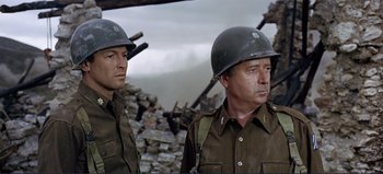 Movie still from “Patton” (1970), directed by Franklin J. Schaffner – Two men in military fatigues standing next to a pile of rubble; Medium shot, Over the shoulder angle