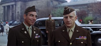 Movie still from “Patton” (1970), directed by Franklin J. Schaffner – A couple of men in uniform standing next to each other in front of a car; Medium shot, Low angle