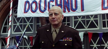 Movie still from “Patton” (1970), directed by Franklin J. Schaffner – A man in a military uniform standing in front of a banner; Medium shot, Low angle
