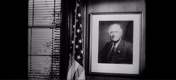 Movie still from “Patton” (1970), directed by Franklin J. Schaffner – A black and white photo of a man in a suit and tie next to an american flag; Close Up shot, Low angle
