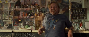 Movie still from “Paul” (2011), directed by Greg Mottola – A man in a t - shirt is smiling for the camera; Medium shot, Over the shoulder angle