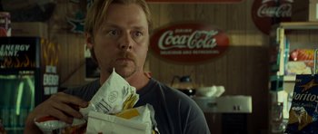 Movie still from “Paul” (2011), directed by Greg Mottola – A man holding a bag in front of a coca - cola sign; Close Up shot, Over the shoulder angle