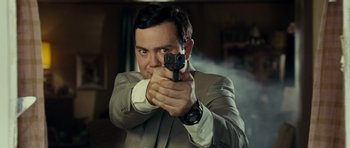 Movie still from “Paul” (2011), directed by Greg Mottola – A man in a suit and tie holding a gun in his hand; Close Up shot, Over the shoulder angle