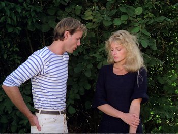 A man and a woman standing next to each other in front of bushes