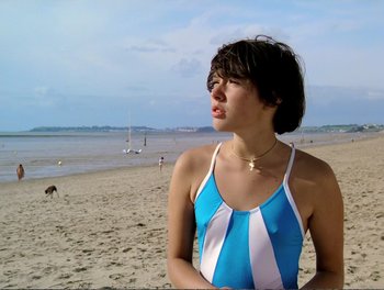 Movie still from “Pauline at the Beach” (1983), directed by Éric Rohmer – A woman in a blue and white bathing suit standing on a beach; Medium shot, High angle