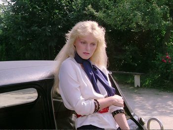A woman in a white shirt leaning against a car