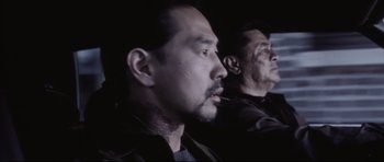 Movie still from “Payback” (1999), directed by Brian Helgeland – A man with a beard smoking a cigarette next to another man; Close Up shot, Over the shoulder angle