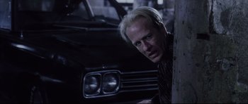 Movie still from “Payback” (1999), directed by Brian Helgeland – A man in a black shirt leaning against a wall; Close Up shot, Low angle