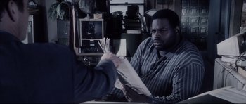 Movie still from “Payback” (1999), directed by Brian Helgeland – A man holding a newspaper in front of another man in a cluttered room; Close Up shot, Over the shoulder angle