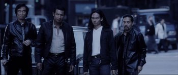 Movie still from “Payback” (1999), directed by Brian Helgeland – A group of men standing next to each other on the street; Medium shot, Low angle
