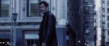 Movie still from “Payback” (1999), directed by Brian Helgeland – A man in a leather jacket standing in front of a tall building; Medium shot, Low angle