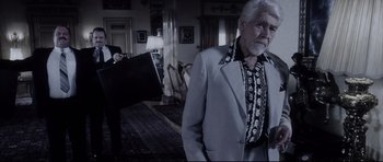 Movie still from “Payback” (1999), directed by Brian Helgeland – An older man in a suit and tie standing in front of a piano in a living room; Medium shot, Over the shoulder angle