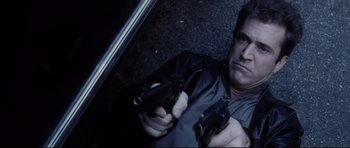 Movie still from “Payback” (1999), directed by Brian Helgeland – A man holding two guns while standing next to a car; Close Up shot, High angle
