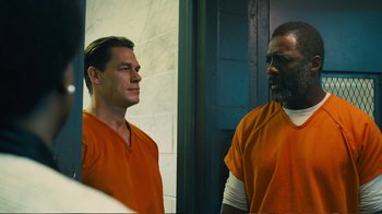 Movie still from “Peacemaker” (2022), created by James Gunn – Two men in orange shirts looking at each other in front of a wall; Medium shot, Low angle