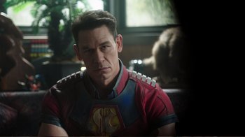 Movie still from “Peacemaker” (2022), created by James Gunn – A man in a red and blue shirt and a monkey in the background; Close Up shot, Over the shoulder angle