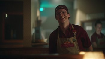 Movie still from “Peacemaker” (2022), created by James Gunn – A man in a hat and apron smiling for the camera; Medium shot, Over the shoulder angle