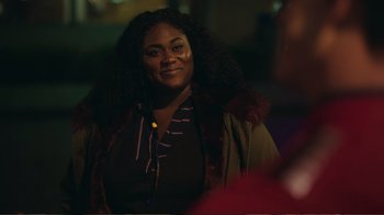 Movie still from “Peacemaker” (2022), created by James Gunn – A black woman with long curly hair wearing a brown jacket; Close Up shot, Over the shoulder angle