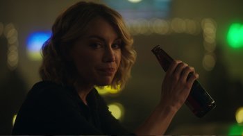 Movie still from “Peacemaker” (2022), created by James Gunn – A woman holding a bottle of beer in her hand; Close Up shot, Over the shoulder angle