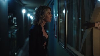 Movie still from “Peacemaker” (2022), created by James Gunn – A woman standing in front of a window in a dark room; Close Up shot, Over the shoulder angle