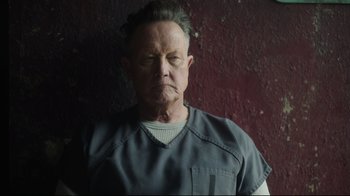 Movie still from “Peacemaker” (2022), created by James Gunn – An older man wearing a gray shirt and a black shirt; Close Up shot, Low angle