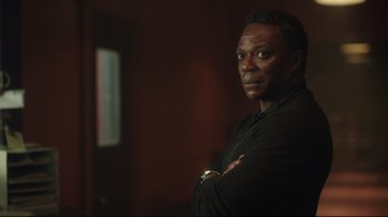 Movie still from “Peacemaker” (2022), created by James Gunn – A man with his arms crossed in front of a wall; Close Up shot, Low angle