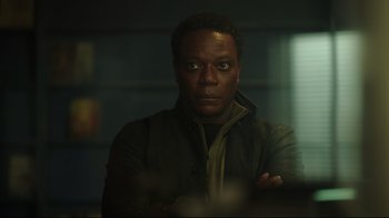 Movie still from “Peacemaker” (2022), created by James Gunn – A black man with his arms crossed in a dark room; Close Up shot, Over the shoulder angle