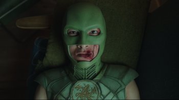 Movie still from “Peacemaker” (2022), created by James Gunn – A man in a green costume with a face covered in blood; Close Up shot, Overhead angle