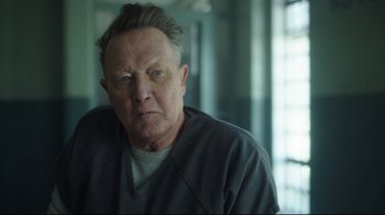 Movie still from “Peacemaker” (2022), created by James Gunn – An older man in a gray shirt is looking at the camera; Close Up shot, Over the shoulder angle