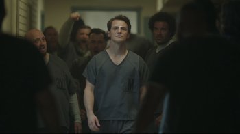 Movie still from “Peacemaker” (2022), created by James Gunn – A group of people in a room with one man in a gray shirt; Medium shot, Over the shoulder angle